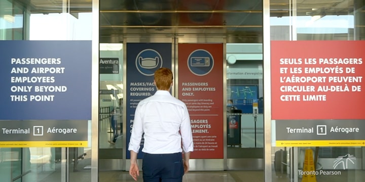 Person entering Pearson Airport through sliding doors with posters on the glass about Healthy Airport