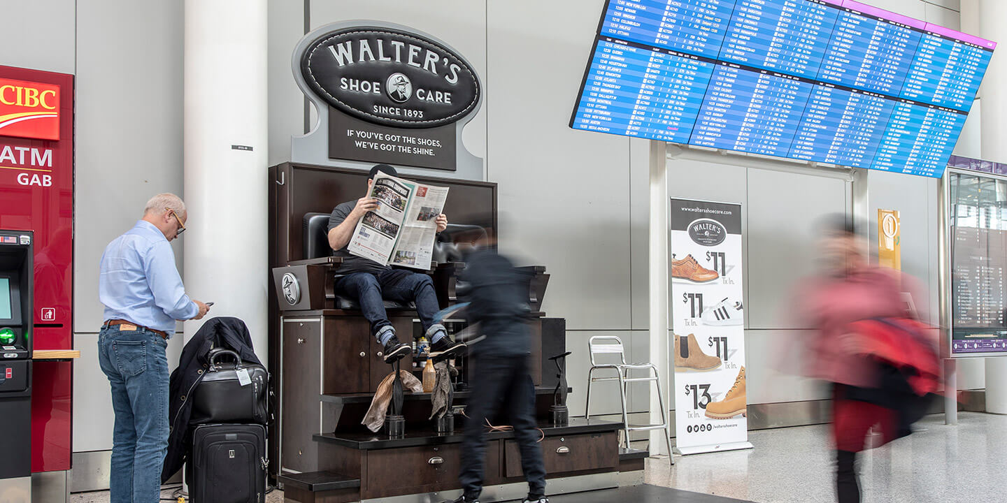 Un homme lit un journal tout en se faisant cirer les chaussures à un kiosque Walter’s Shoe Care